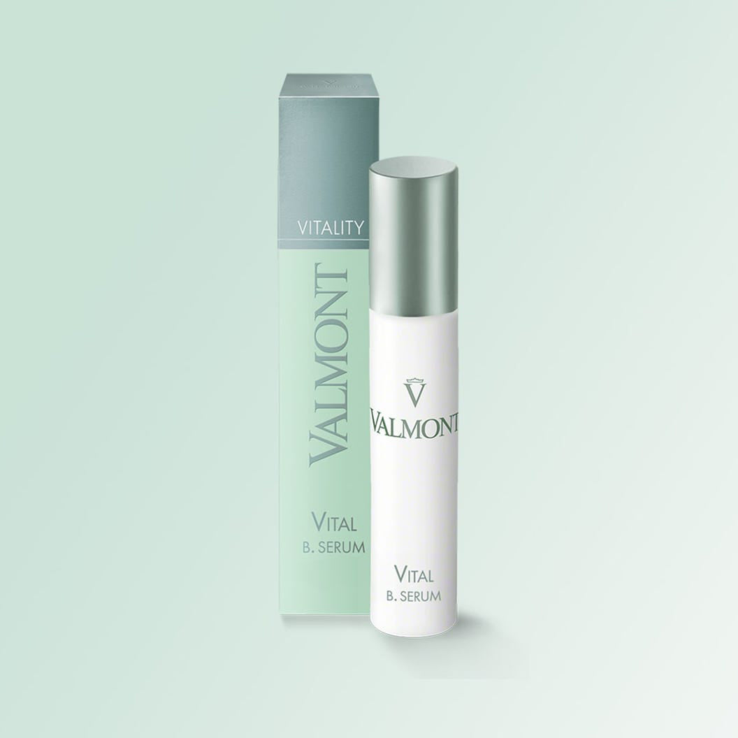 A white bottle of VALMONT Vital B. Serum is placed before its matching green and white box labeled Vitality, set against a pale green background.