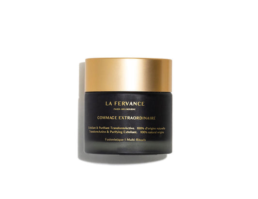 A black and gold jar of Gommage Extraordinaire skin exfoliating emulsion with gold text and a matte finish, photographed on a white background with a soft shadow. Made in France.