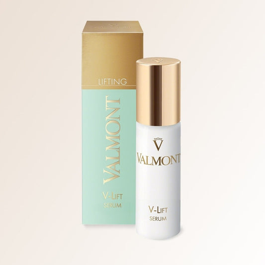 A bottle of V-Lift Serum with a gold cap is placed in front of its matching mint green and gold box, both featuring the Valmont logo and “V-Lift Serum” text on a light beige background.